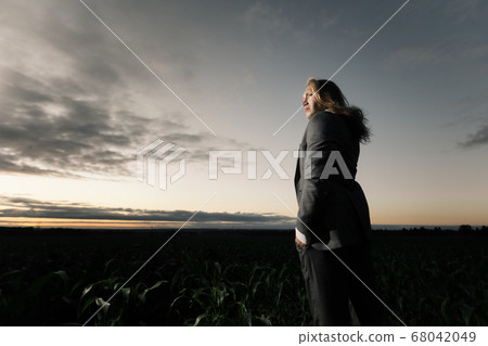 young stylish guy stands in a field in a gray suit at sunset. Blond with long hair in a cornfield young stylish guy stands in a field in a gray suit at sunset. Blond with long hair in a cornfield 68042049