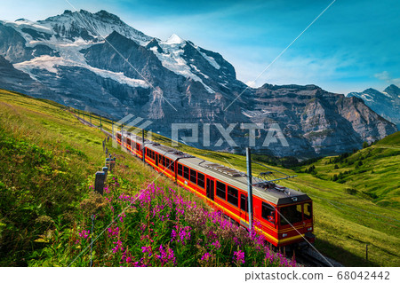 Electric passenger train and snowy Jungfrau mountains in background, Switzerland Electric passenger train and snowy Jungfrau mountains in background, Switzerland 68042442