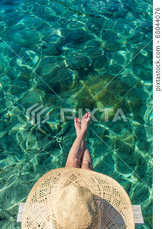 Graphic image of top down view of woman wearing big summer sun hat relaxing on small wooden pier by clear turquoise sea Graphic image of top down view of woman wearing big summer sun hat relaxing on small wooden pier by clear turquoise sea 68044076