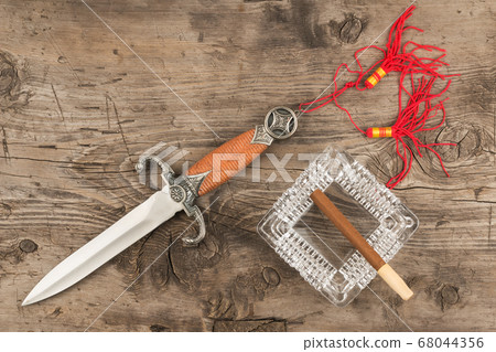 Cigar in ashtray and dagger on old wooden board. Cigar in ashtray and dagger on old wooden board. 68044356