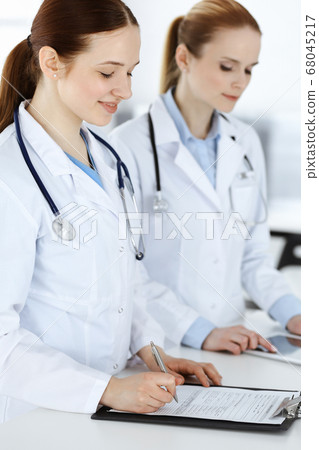 Woman-doctor at work. Female physician or internal student filling up medical documents or prescription while standing in clinic reception desk. Data in medicine 68045217