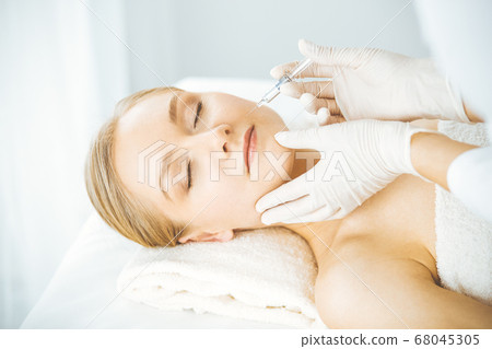 Beautician doctor doing beauty procedure with syringe to blonde female face. Cosmetic medicine, beauty injections concept Beautician doctor doing beauty procedure with syringe to blonde female face. Cosmetic medicine, beauty injections concept 68045305