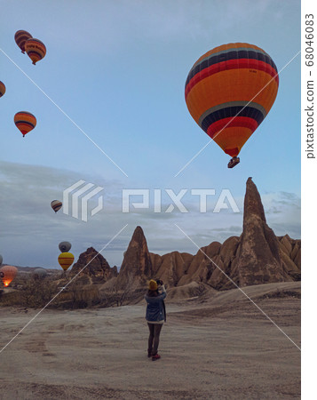 Young woman watching hot air balloons at early morning with rocky landscape in Cappadocia, Turkey 68046083