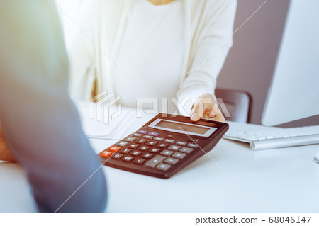 Accountant checking financial statement or counting by calculator income for tax form, hands close-up. Business woman sitting and working with colleague at the desk in office. Audit concept Accountant checking financial statement or counting by calculator income for tax form, hands close-up. Business woman sitting and working with colleague at the desk in office. Audit concept 68046147