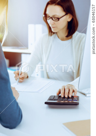 Accountant checking financial statement or counting by calculator income for tax form, hands close-up. Business woman sitting and working with colleague at the desk in office. Audit concept Accountant checking financial statement or counting by calculator income for tax form, hands close-up. Business woman sitting and working with colleague at the desk in office. Audit concept 68046157
