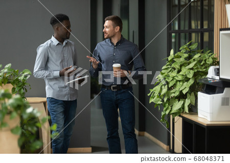 Diverse friendly male partners talking walking in office hallway Diverse friendly male partners talking walking in office hallway 68048371
