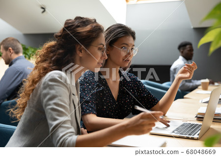 Female asian mentor teaching caucasian intern explaining online project Female asian mentor teaching caucasian intern explaining online project 68048669