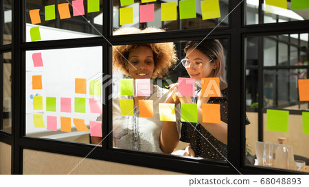 Happy african and asian businesswomen working with sticky notes Happy african and asian businesswomen working with sticky notes 68048893