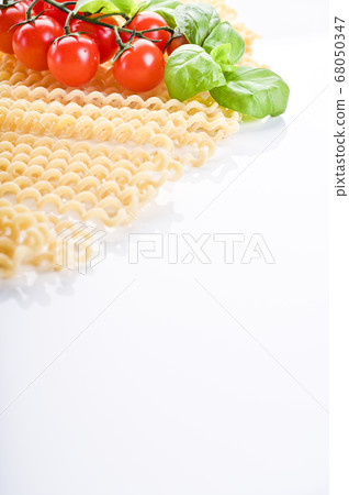Fusilli lunghi bucati . Long curly pasta on a white plate, with fresh basil leaves and cherry 68050347