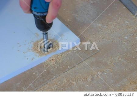 Man drill round hole for door hinges in chipboard usinf electric drill, closeup. 68053137