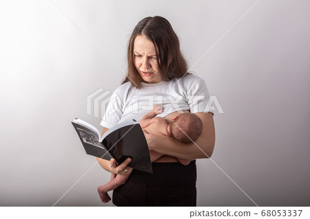 Beautiful young mother breastfeeding a baby while reading a black book Beautiful young mother breastfeeding a baby while reading a black book 68053337