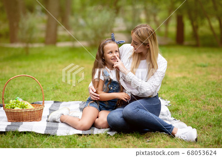 Young Mother Touching Daughter's Nose Having Picnic Outside In Park Young Mother Touching Daughter's Nose Having Picnic Outside In Park 68053624