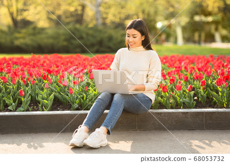 Asian girl using laptop, sitting on parapet in park Asian girl using laptop, sitting on parapet in park 68053732