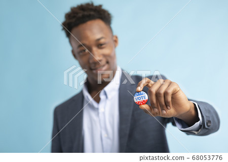 African american man showing vote pin, blurred background African american man showing vote pin, blurred background 68053776