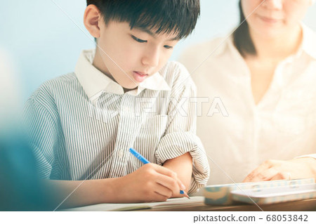 An adult watching a boy studying 68053842