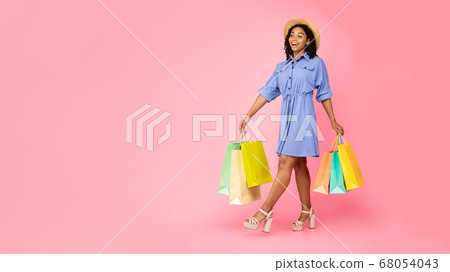 Black Lady Walking Carrying Colorful Shoppers On Pink Studio Background Black Lady Walking Carrying Colorful Shoppers On Pink Studio Background 68054043