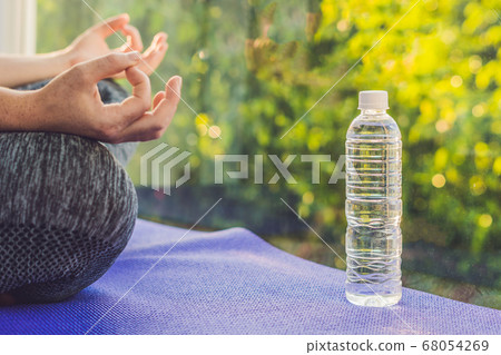 hand of a woman meditating in a yoga pose on a rug for yoga and a bottle of water hand of a woman meditating in a yoga pose on a rug for yoga and a bottle of water 68054269