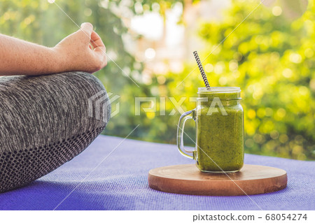 Closeup of a woman's hands during meditation with a green smoothies of spinach, orange and banana 68054274