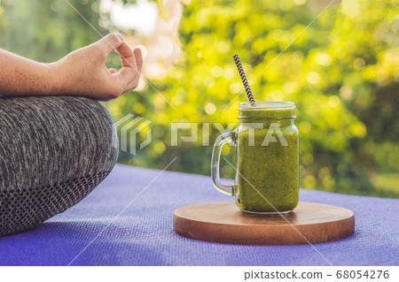 Closeup of a woman's hands during meditation with a green smoothies of spinach, orange and banana Closeup of a woman's hands during meditation with a green smoothies of spinach, orange and banana 68054276