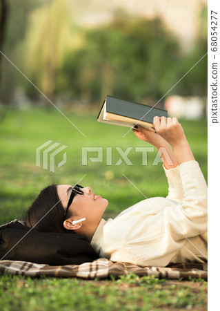 Girl reading book lying in warm summer grass Girl reading book lying in warm summer grass 68054277