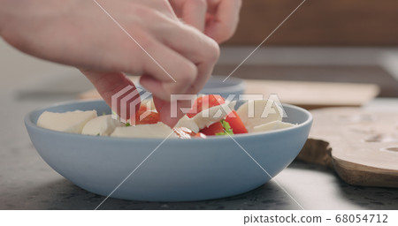 making salad with frisee lettuce, tomatoes amd mozzarella in a blue bowl on kitchen countertop 68054712
