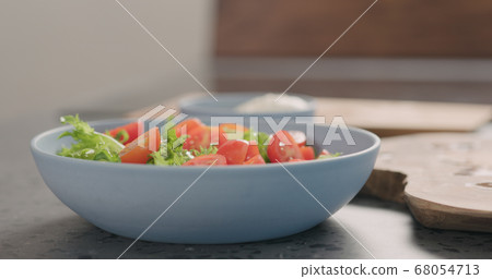 making salad with frisee lettuce, tomatoes amd mozzarella in a blue bowl on kitchen countertop 68054713