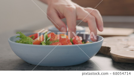 making salad with frisee lettuce, tomatoes amd mozzarella in a blue bowl on kitchen countertop making salad with frisee lettuce, tomatoes amd mozzarella in a blue bowl on kitchen countertop 68054714