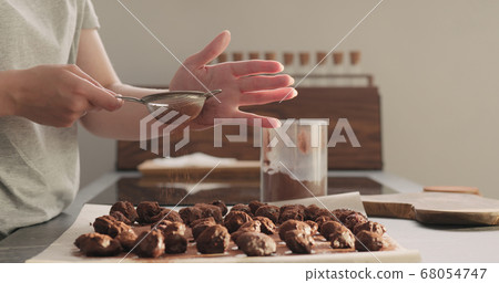 young woman sprinkle cocoa powder on chocolate truffles young woman sprinkle cocoa powder on chocolate truffles 68054747