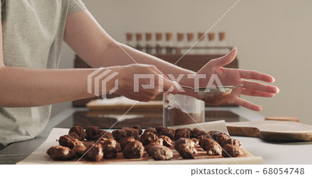young woman sprinkle cocoa powder on chocolate truffles young woman sprinkle cocoa powder on chocolate truffles 68054748