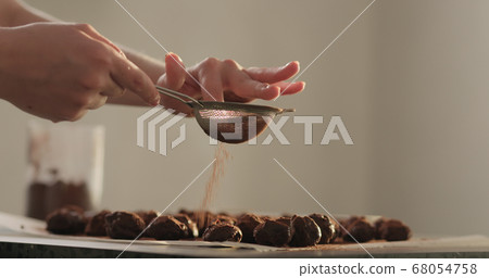 young woman sprinkle cocoa powder on chocolate truffles young woman sprinkle cocoa powder on chocolate truffles 68054758