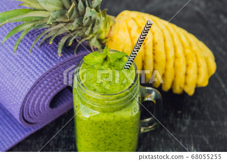 Green smoothies made of spinach and pineapple and a yoga mat. Healthy eating and sports concept 68055255
