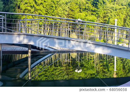 in a city park a metal bridge over a river at dawn. 68056038