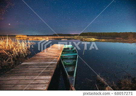 Belarus, Eastern Europe. Real Night Sky Stars Above Old Pier With Moored Wooden Fishing Boat. Natural Starry Sky And Countryside Landscape With Lake River In Early Spring Night. Russian Nature 68057271