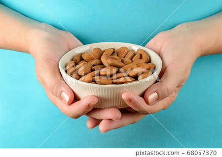 Caucasian woman hands hold beige ceramic bowl with raw almonds. 68057370