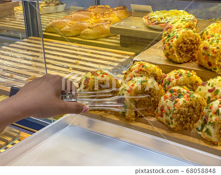 Customer's hand picking pork floss roll by tongs at bakeshop 68058848