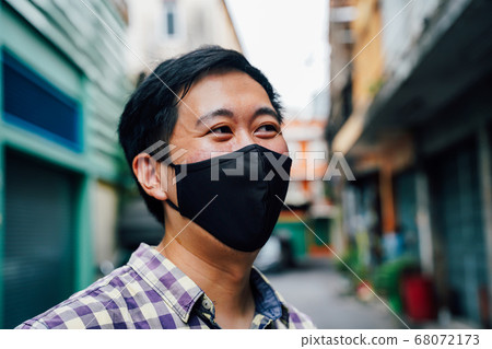 Portrait of one Asian smiling man wearing a face mask on neighborhood street in Thailand Portrait of one Asian smiling man wearing a face mask on neighborhood street in Thailand 68072173