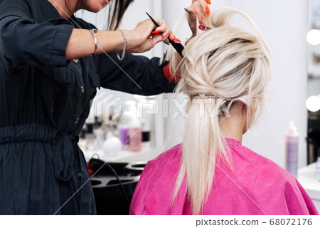 Hands of a hair stylist with a comb make a hairstyle for a blonde girl 68072176