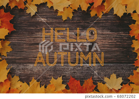 Greeting text Hello Autumn on wooden background with frame of maple leaves 68072202