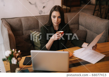 Busy young businesswoman works with paper documents in cafe sitting at table with laptop. 68077413