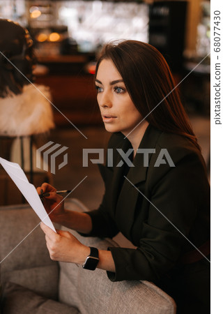 Portrait of beautiful young woman wearing stylish clothes in restaurant holding paper documents. 68077430