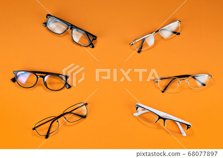 Different types of glasses on an orange background close up. Glasses with rectangular and round frames.  68077897