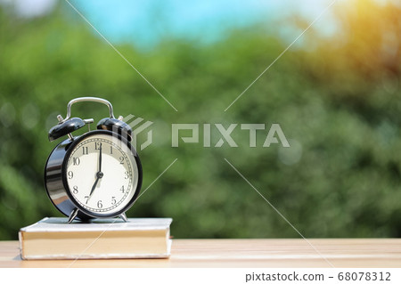 Vintage alarm clock with white book on wooden desk with green nature background Vintage alarm clock with white book on wooden desk with green nature background 68078312