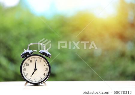 Vintage alarm clock on wooden desk with green nature and sunlight background Vintage alarm clock on wooden desk with green nature and sunlight background 68078313