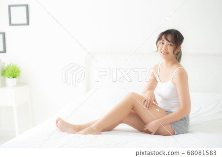 Beautiful young asian woman sitting on a bed stroking legs with soft smooth skin in the bedroom. 68081583