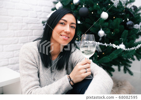 A young woman sits near a Christmas tree, holding A young woman sits near a Christmas tree, holding 68082595