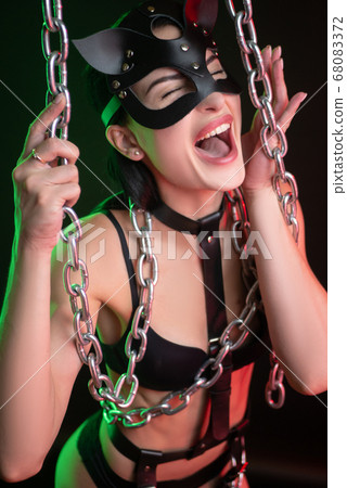 Hot brunette posing on a dark background in a belt and a cat mask with chains dancing a Striptease Hot brunette posing on a dark background in a belt and a cat mask with chains dancing a Striptease 68083372