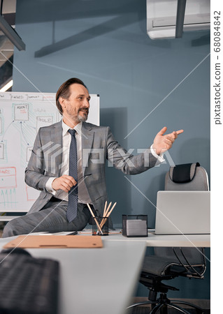 Handsome man sitting on table in office Handsome man sitting on table in office 68084842