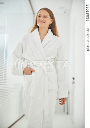 Smiling cheerful female wearing white bathrobe walking in the corridor of beauty center 68085055