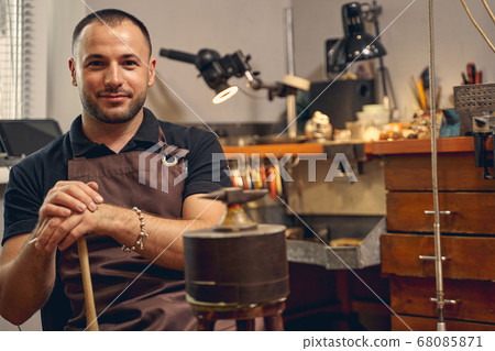Smiling jeweler sitting in front of the anvil 68085871