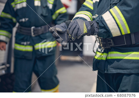 Portrait of strong hands of firefighter standing in front of another man Portrait of strong hands of firefighter standing in front of another man 68087076